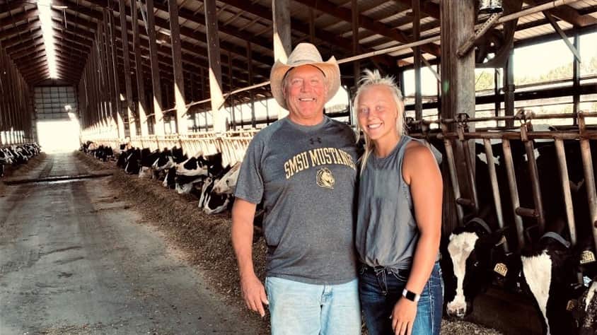 Sadie Stelter and her father, David, posing for a photo in a barn full of dairy cows