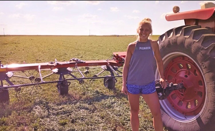 Sadie Stelter takes a break next to a hay tedder