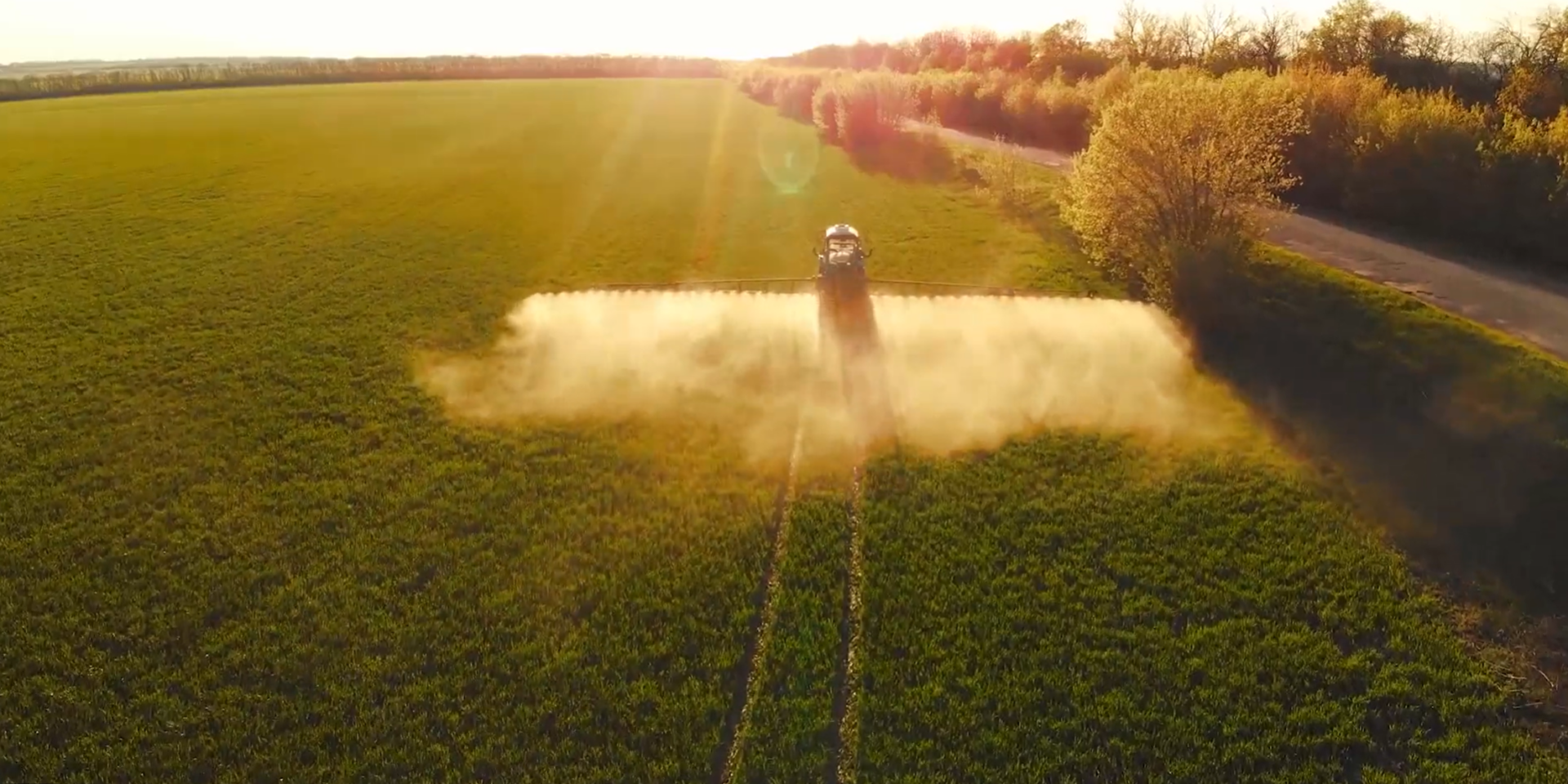 Sprayer applying product across a field at sunset